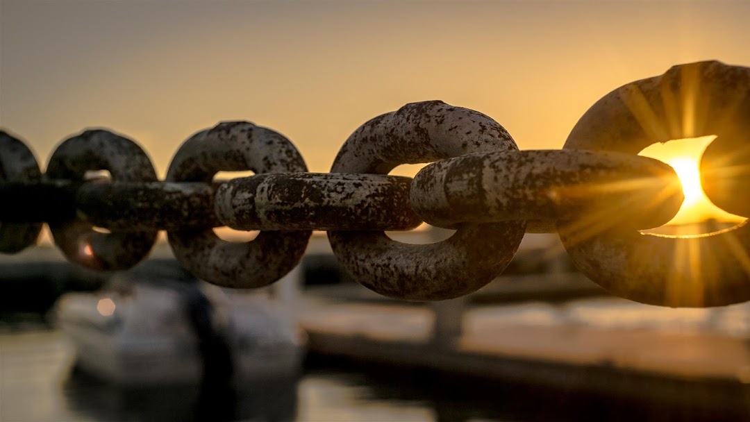 Close-up of a rusty anchor chain backlit by a golden sunset over a marina
